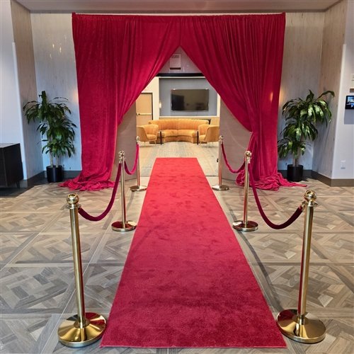 a-red-carpet-entrance-with-gold-stanchions-red-rope-barriers-and-a-draped-red-fabric-archway-leading-into-a-modern-venue